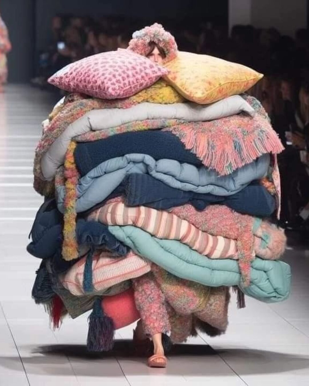 Tendances mode 2028 : silhouette enveloppée d'un empilement de coussins et plaids texturés, esthétique Soft Protection