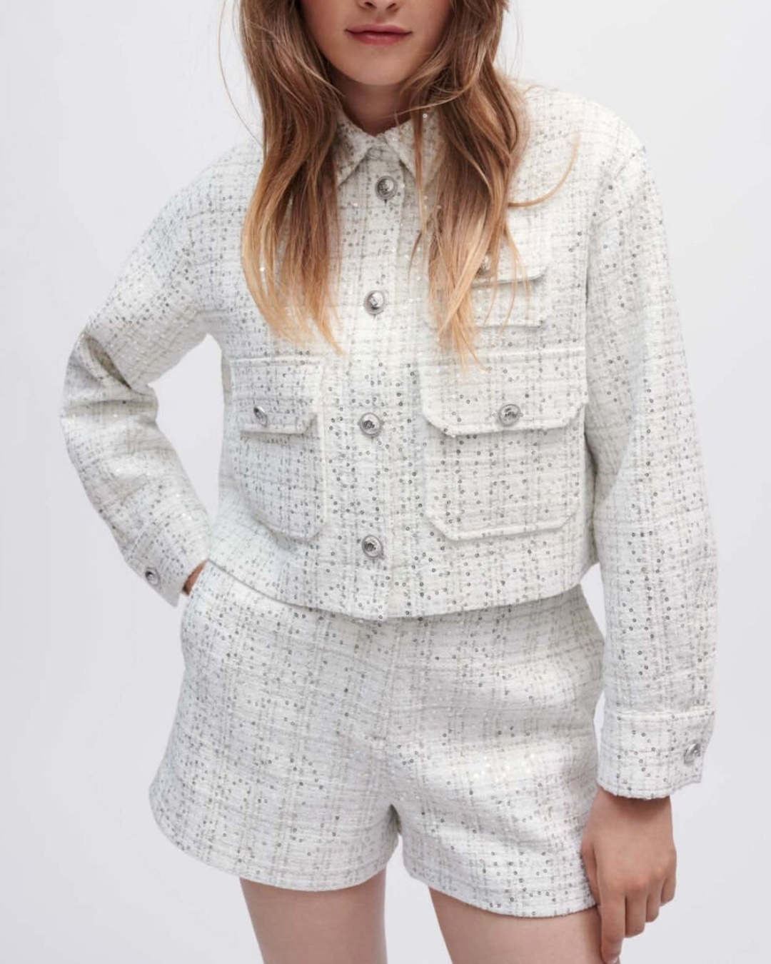 Veste courte Maje en tweed blanc à boutons argentés, portée avec un short coordonné